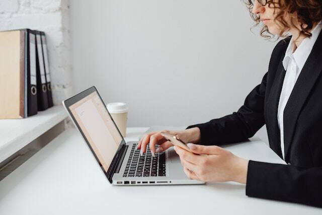 person in a black suit jacket working on their laptop and holding their phone